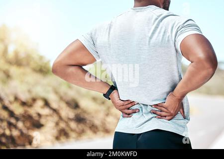 Nahkampf-FIT-Mann mit gemischtem Rennen hält sich den Rücken vor Schmerzen, während er draußen trainiert. Nicht erkennbarer männlicher Sportler, der eine Muskelverletzung am Körper erlitten hat Stockfoto