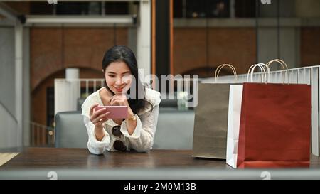 Attraktive, stilvolle Frau, die im Café im Freien auf dem Mobiltelefon eine Massage tippt Stockfoto