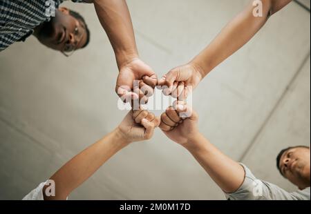 Nahaufnahme von kreativen Geschäftsleuten, die ihre Fäuste von unten zusammenbringen. Eine vielfältige Gruppe von Geschäftsleuten, die in einer Zusammenkunft zusammenstehen Stockfoto