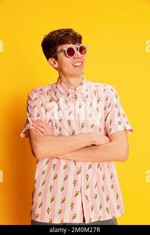 Porträt eines verblüfften jungen Mannes in modischer Brille, die isoliert auf hellgelbem Hintergrund lächelt. Jugendkultur, positive Emotionen Stockfoto