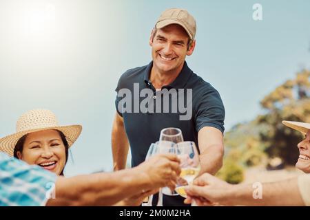 Vielfältige Gruppe von Freunden, die mit Weingläsern auf dem Weinberg anstoßen. Eine glückliche Gruppe von Menschen, die sich während der Weinprobe auf dem Bauernhof zusammengesessen haben Stockfoto