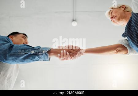 Zwei Bekleidungsdesigner schütteln sich die Hand, während sie in einem Geschäft zusammenarbeiten. Eine reife weiße Frau und ein junger asiatischer Mann, die sich gegenseitig die Hand schütteln Stockfoto