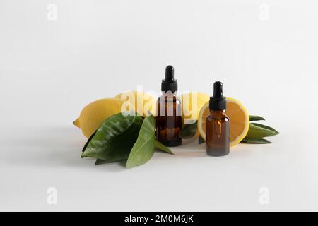 Zwei Kosmetikflaschen mit einer Pipette und einem Serum auf Basis von ätherischem Zitronenöl auf weißem Hintergrund mit reifen Früchten. Verjüngungseffekt. Vitamin C Stockfoto