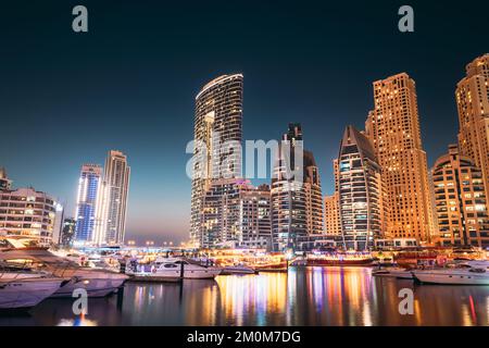 Dubai Marina Port, VAE, Vereinigte Arabische Emirate - 19. Mai 2021: Anlegesteg mit vielen festgetäuten Yachten, Sightseeing-Boot in Abendnächte Illuminationen. Nacht Stockfoto