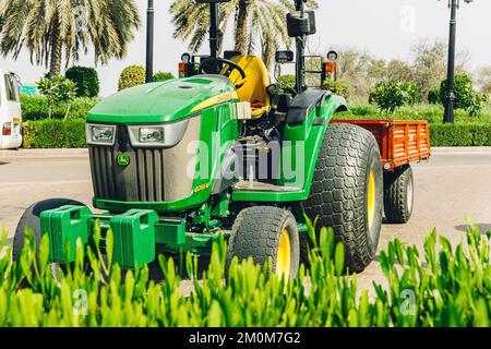 Dubai, Vereinigte Arabische Emirate, Vereinigte Arabische Emirate - 25. Mai 2021: John Deere Kompakt-Utility-Traktor 4066M mit Anhänger auf dem Weg in Park geparkt. Kompakter Utility-Traktor Stockfoto