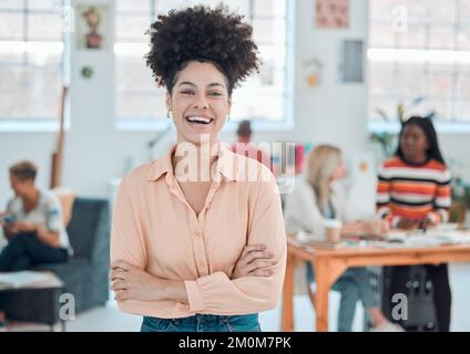 Junge, fröhliche Geschäftsfrau gemischter Rassen, die im Büro mit gekreuzten Armen stand. Selbstbewusste, hispanische Managerin mit lockigem Afro-Lächeln Stockfoto