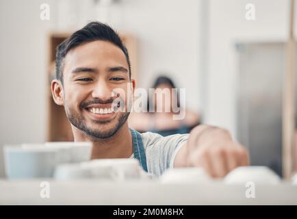 Ein glücklicher hispanischer Kellner, der in einem Café ein heißes Getränk mit einer Kaffeemaschine zubereitet. Ein glücklicher Barista bereitet ein warmes Getränk zu, um Gäste in einem zu bedienen Stockfoto