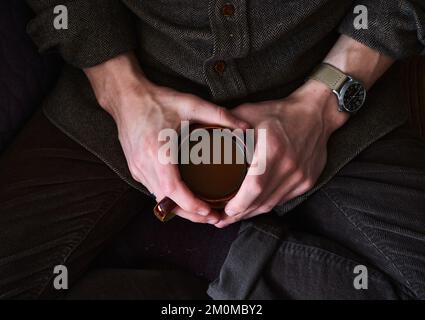 Die Hände eines Mannes, der eine heiße Tasse dunklen Kaffees hält Stockfoto