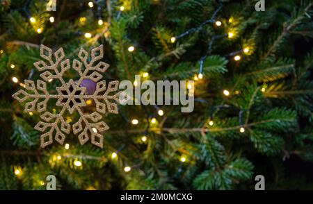 Weihnachtliche goldene Schneeflocke auf Weihnachtstanne und Bokeh-Lichter Hintergrund, Kopierbereich. Weihnachtsdekoration im Winter, Kartenvorlage Stockfoto