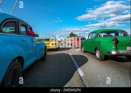 Eine lange Schlange von Autos hielt am Meer an einem sonnigen Tag auf einer Straße, im Vordergrund mit amerikanischen Oldtimern, Leute warteten an der Seite Stockfoto