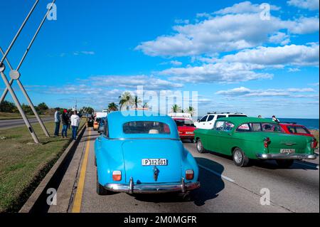 Eine lange Schlange von Autos hielt am Meer an einem sonnigen Tag auf einer Straße, im Vordergrund mit amerikanischen Oldtimern, Leute, die am Straßenrand warteten Stockfoto