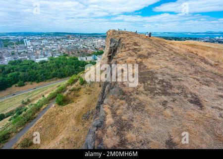 Edinburgh, Schottland-August 01 2022: Besucher, die auf Arthurs Sitz klettern, stehen am Abgrund einer hohen vertikalen Klippe und staunen über Edinburgh Stockfoto