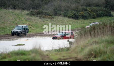 Drei Land Rover Discovery 4x4 Geländefahrzeuge, die durch tiefes Wasser und Schlamm auf offener Landschaft in Wiltshire UK gefahren werden Stockfoto