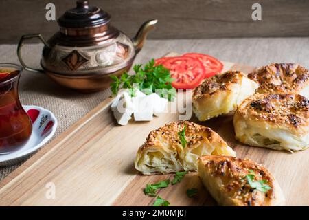 Traditionell köstliches türkisches Yufka mit Käsefüllung (türkischer Name: Rosengebäck), rosenförmiges Gebäck und Tee auf Holzbrett. Stockfoto