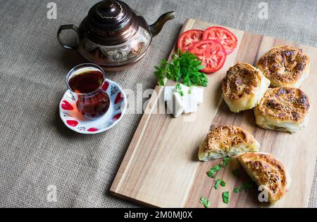 Traditionell köstliches türkisches Yufka mit Käsefüllung (türkischer Name: Rosengebäck), rosenförmiges Gebäck und Tee auf Holzbrett. Stockfoto