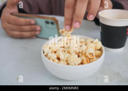 Junge Frauen essen Popcorn und halten ein Smartphone Stockfoto