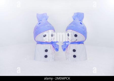 Zwei Schwalben stehen auf Schnee. Handgefertigtes Spielzeug mit blauer Stoffmütze und Schal. Schneeflocken-Nahaufnahme Stockfoto