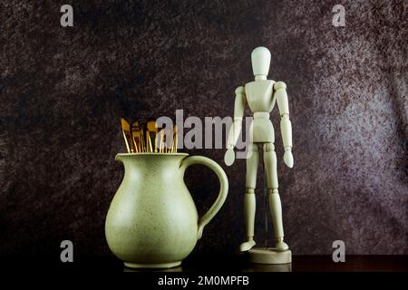 Weinkanne aus Steingut mit Malpinseln und Schaufensterpuppe auf einem polierten Holzregal Stockfoto