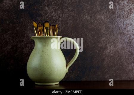 Keramikkrug und Malpinsel von Künstlern auf einem polierten Holzregal Stockfoto