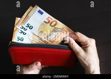 Euro-Banknoten in roter Brieftasche in zerknitterten Händen älterer Frauen. Das Konzept der Renten- und Unterstützungsleistungen, des Sparens, des Ruhestands in Europa Stockfoto