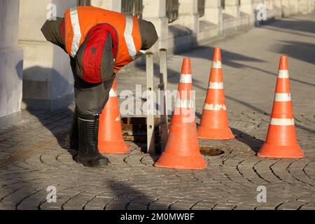 Arbeiter, der über der offenen Abwasserluke auf der Winterstraße stand. Konzept der Abwasserreparatur, der unterirdischen Versorgung, der Kabelverlegung Stockfoto