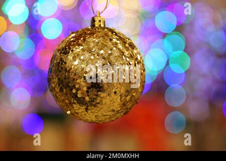 Weihnachtsspielzeug, goldglänzender Ball auf verschwommenem weihnachtlichem Hintergrund. Neujahrsdekoration Stockfoto