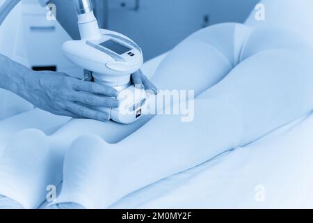 Eine Frau in einem speziellen weißen Anzug bekommt eine Anti-Cellulite-Massage für die Beine in einem Spa-Salon. LPG und Körperkonturierungsbehandlung in der Klinik. Stockfoto