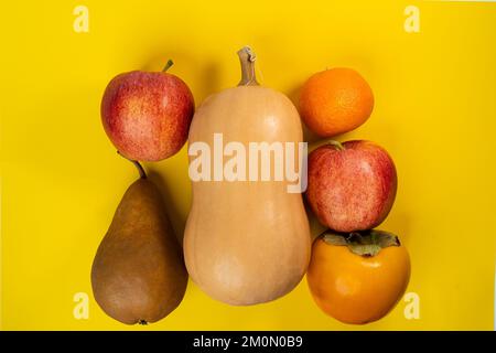 Kürbis, Apfel, Birne, Mandarine und Persimone auf gelbem Hintergrund Stockfoto