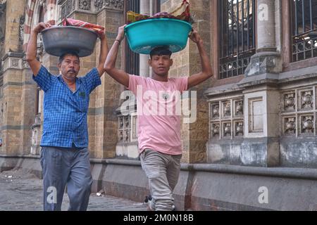 Zwei Träger mit Fischtellern auf dem Kopf, vor dem Chhatrapati Shivaji Maharaj Terminus (CMST) in Mumbai, Indien, um die Tabletts mit dem Zug zu transportieren Stockfoto