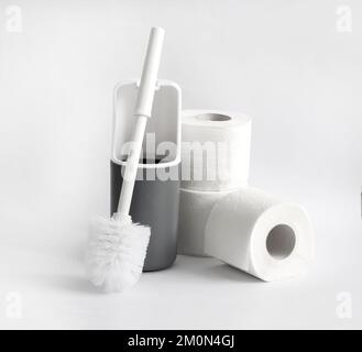 Toilettenbürste aus weißem und grauem Kunststoff und Toilettenpapierrolle auf weißem Hintergrund Stockfoto