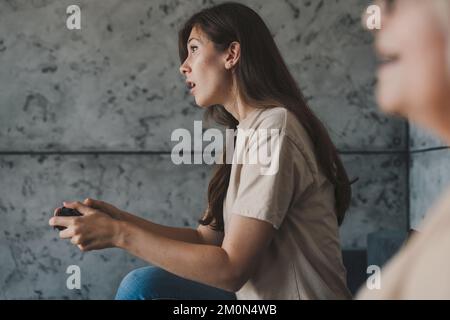 Seniorenmutter und -Tochter spielen gern Videospiele, sitzen auf dem Sofa im Wohnzimmer und verbringen gern Zeit zusammen. Gaming-Unterhaltung und -Technik Stockfoto