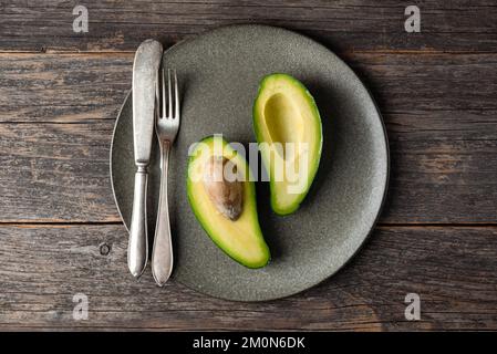 Zwei Hälften Avocado auf dem Teller. Konzept des Essens gesunder, veganer Diät. Draufsicht, Kopierbereich Stockfoto