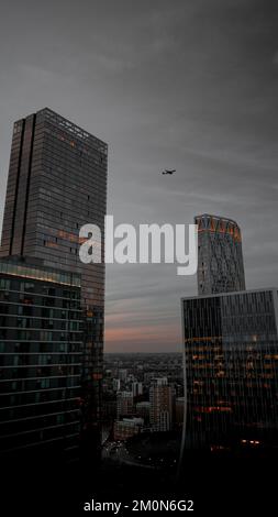 Eine vertikale Aufnahme eines Flugzeugs, das während des Sonnenuntergangs über Canary Wharf fliegt Stockfoto