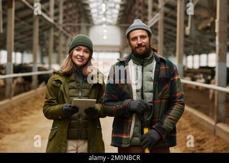 Porträt eines jungen Bauernpaares, das vor der Kamera lächelt und mit Rindern auf dem Bauernhof zusammenarbeitet Stockfoto