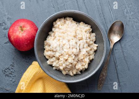 Gerollter Haferflocken, gekochter Haferbrei in Schüssel, serviert mit rotem Apfel. Gesundes veganes Diät-Frühstück. Tabellenansicht, Kopierbereich für Design oder Text Stockfoto