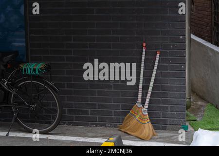 Zwei mit farbigem Faden geschmierte Strohbesen stehen an der Wand. Stockfoto