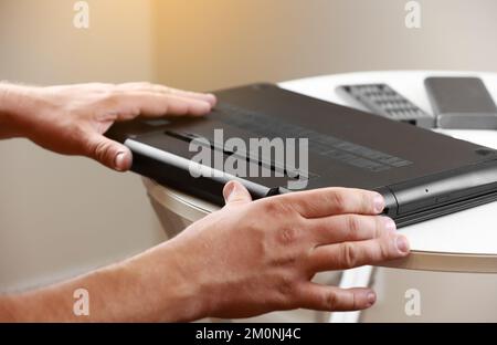 Die Hände des Reparaturmanns, der den Akku aus dem Laptop entfernt. Computerservice- und Reparaturkonzept. Demontage des Laptops in der Reparaturwerkstatt. Elektronische Entwicklung Stockfoto