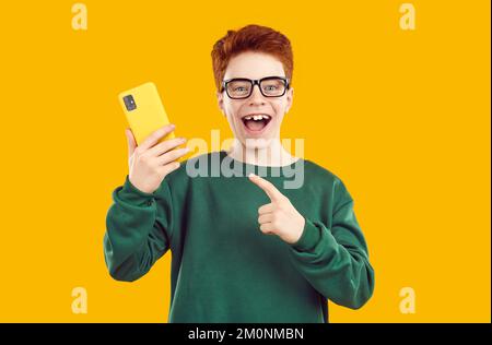 Ein glücklicher, erstaungener Junge, der mit dem Finger auf das Smartphone zeigt Stockfoto