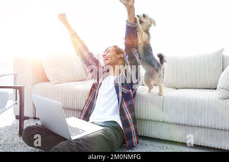 Happy Guy frohlockt mit seinem Hund sitzt in der Nähe der Couch im Wohnzimmer. Stockfoto