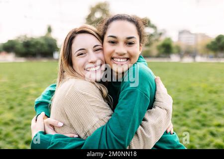 Porträt von glücklichen jungen, multiethnischen, weiblichen Freunden, die sich im Freien umarmen Stockfoto