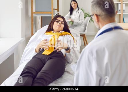 Junge Frau liegt auf der medizinischen Couch im Untersuchungsraum und sagt etwas zum Arzt. Stockfoto
