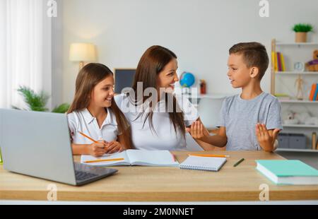 Eine fürsorgliche und freundliche junge Mutter hilft ihren Kindern, ihre Schulaufgaben zu erledigen. Stockfoto