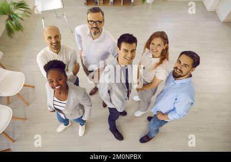 Ein Team glücklicher, multiethnischer Geschäftskollegen, die gemeinsam lächeln und im Büro nach oben schauen. Stockfoto