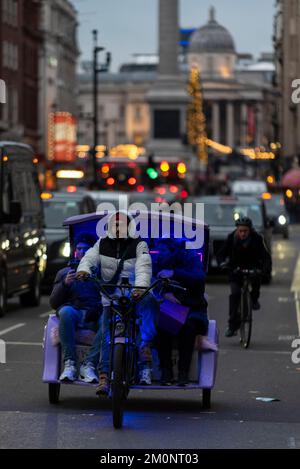 Beleuchtete Rikscha mit Shopper-Passagieren in Whitehall, Westminster, London, Großbritannien, zu Weihnachten am Abend. Fahrradverleih Stockfoto