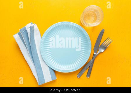 Leerer blauer Teller, Tischtextilien und Besteck auf gelbem Hintergrund. Tabelleneinstellung mit Kopierbereich für Text oder Designelemente Stockfoto