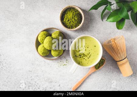 Grüner Tee Matcha latta und Matcha Trüffel auf grauem Steinhintergrund, Draufsicht. Gesunde vegane Energienahrung Stockfoto