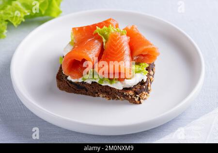 Sandwich mit Lachsfilet und Frischkäse auf einem hellen Holztisch Stockfoto