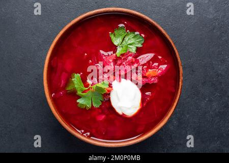 Rote-Bete-Borscht-Suppe mit saurer Sahne in einer Schüssel, isoliert auf einem Tisch aus schwarzem Beton. Draufsicht Stockfoto