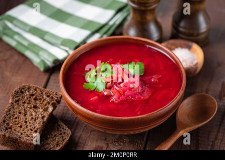 Fleischlose Borschtsch-Suppe serviert mit Roggenbrot auf Holztisch, ukrainische Kulturspeisen Stockfoto