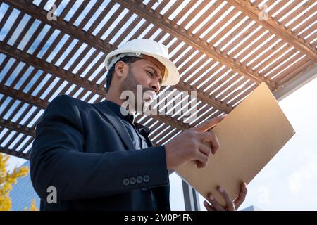 Afroamerikanischer Geschäftsführer mit Bauhelm, der die Baupläne für ein Projekt überprüft. Stockfoto